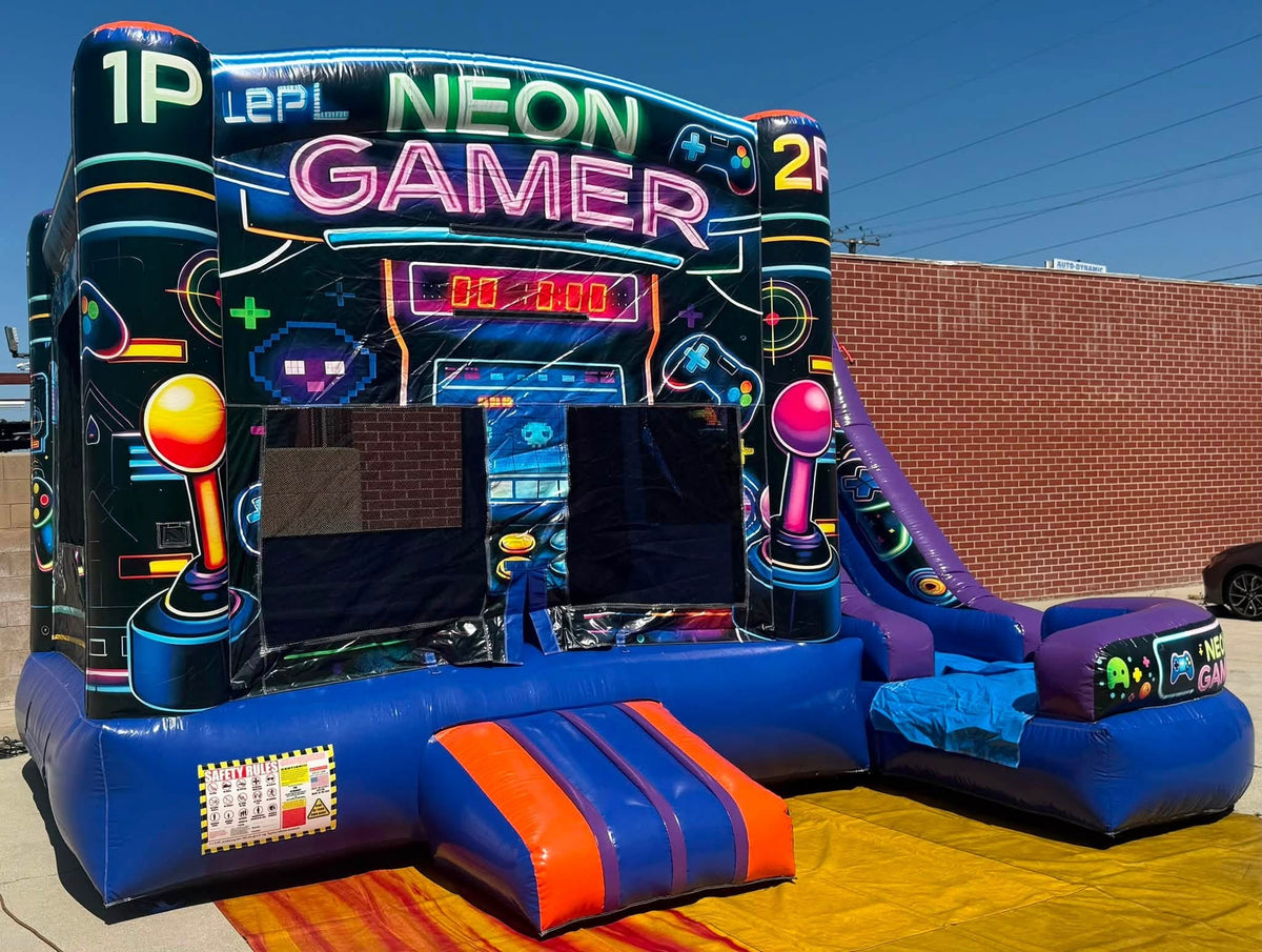 A neon-themed inflatable bounce house with a slide, featuring colorful retro game graphics, arcade-style controls, and the words 'NEON GAMER' on a blue and purple structure outdoors.