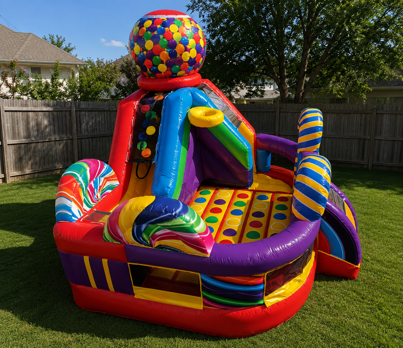 Colorful inflatable slide and play structure on grass with a wooden fence and trees in the background.