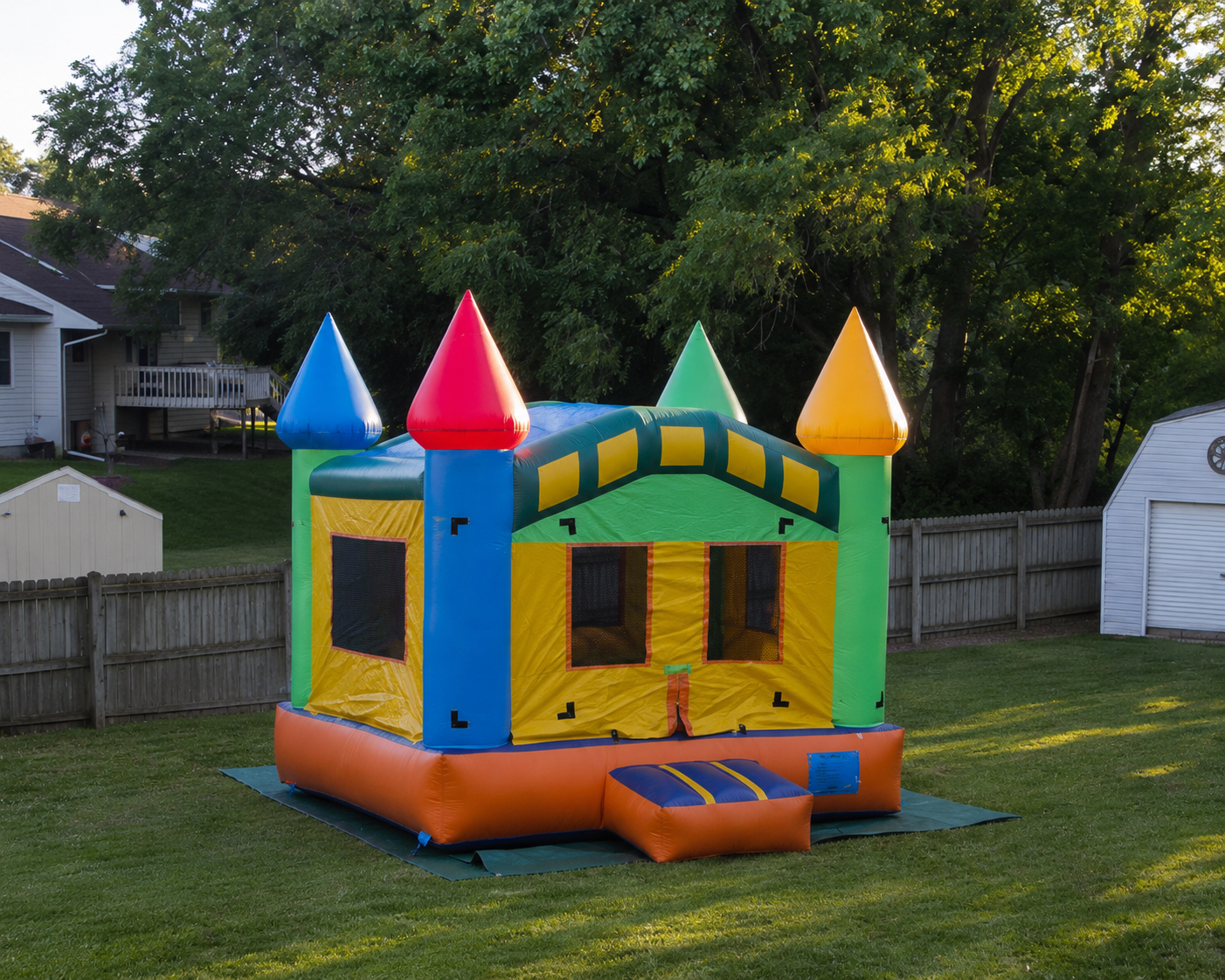 Colorful inflatable bounce house with pyramid-shaped roofs on a grassy backyard.
