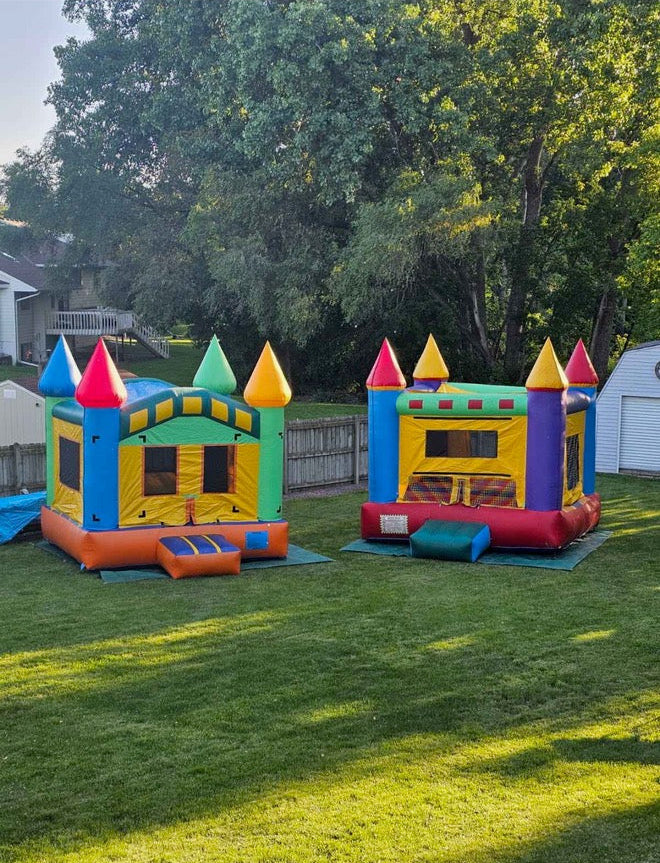 Two colorful inflatable bounce houses on a grassy area with trees in the background.