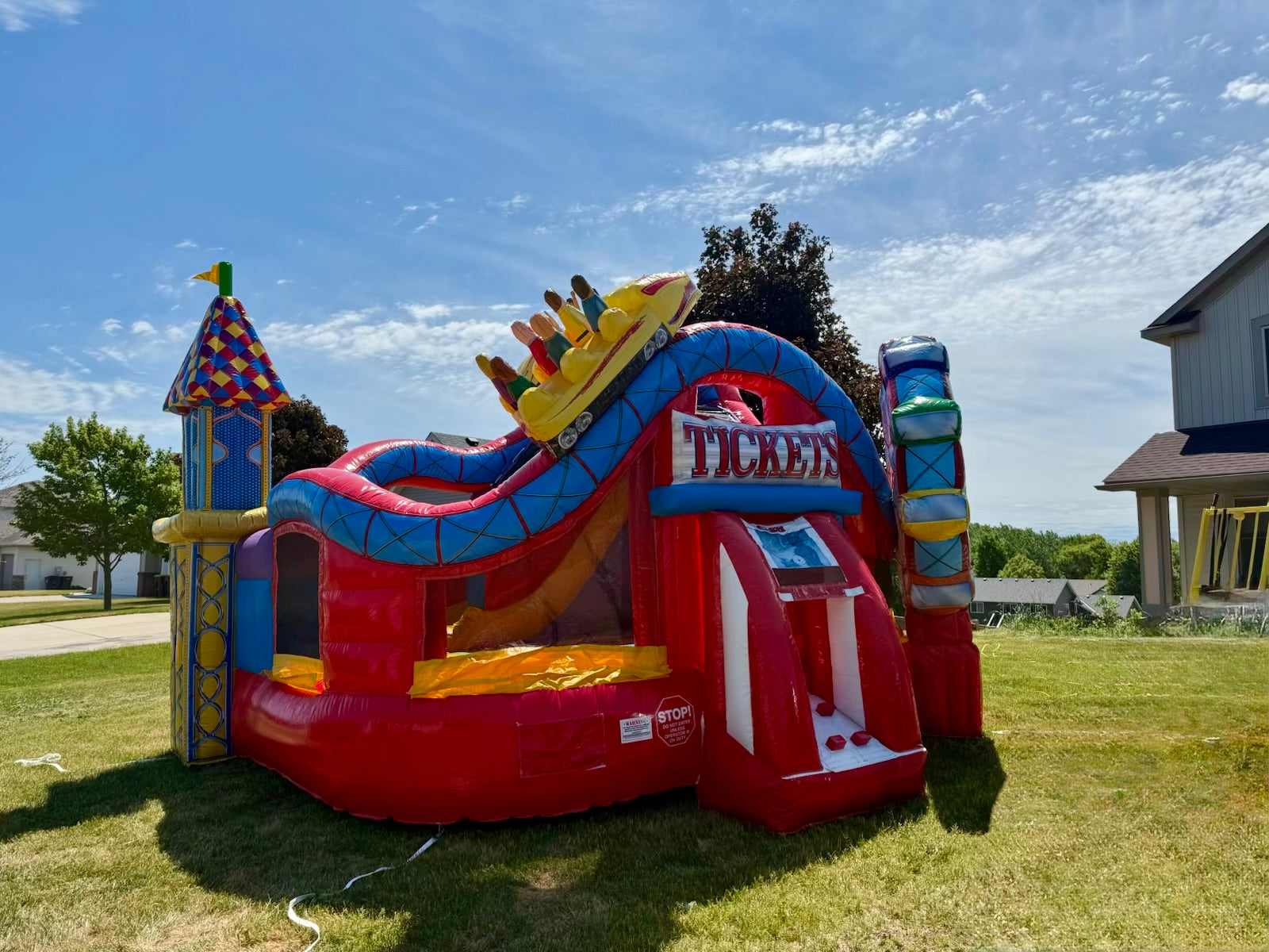 Colorful inflatable bounce house with slide on a grassy area under a blue sky.