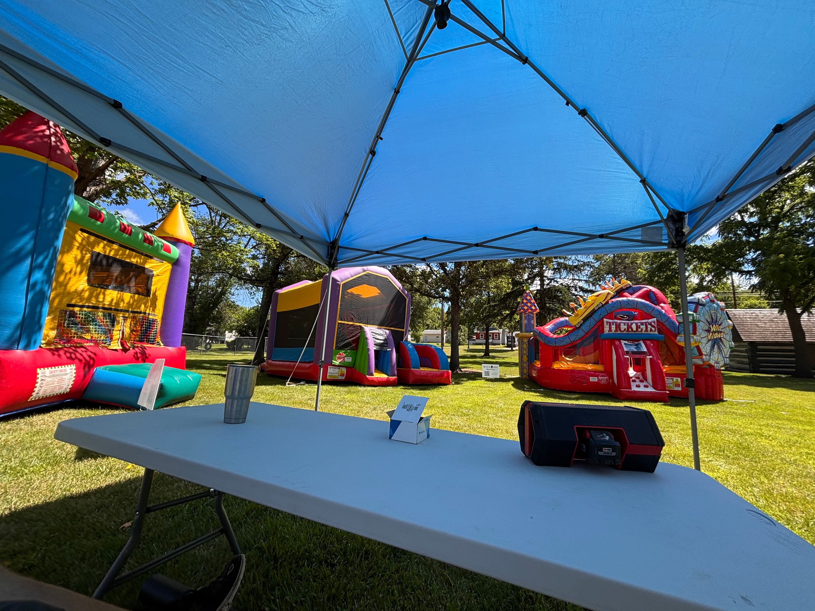 Outdoor setting with inflatable slides and a blue canopy, including a table with a cup and speaker.