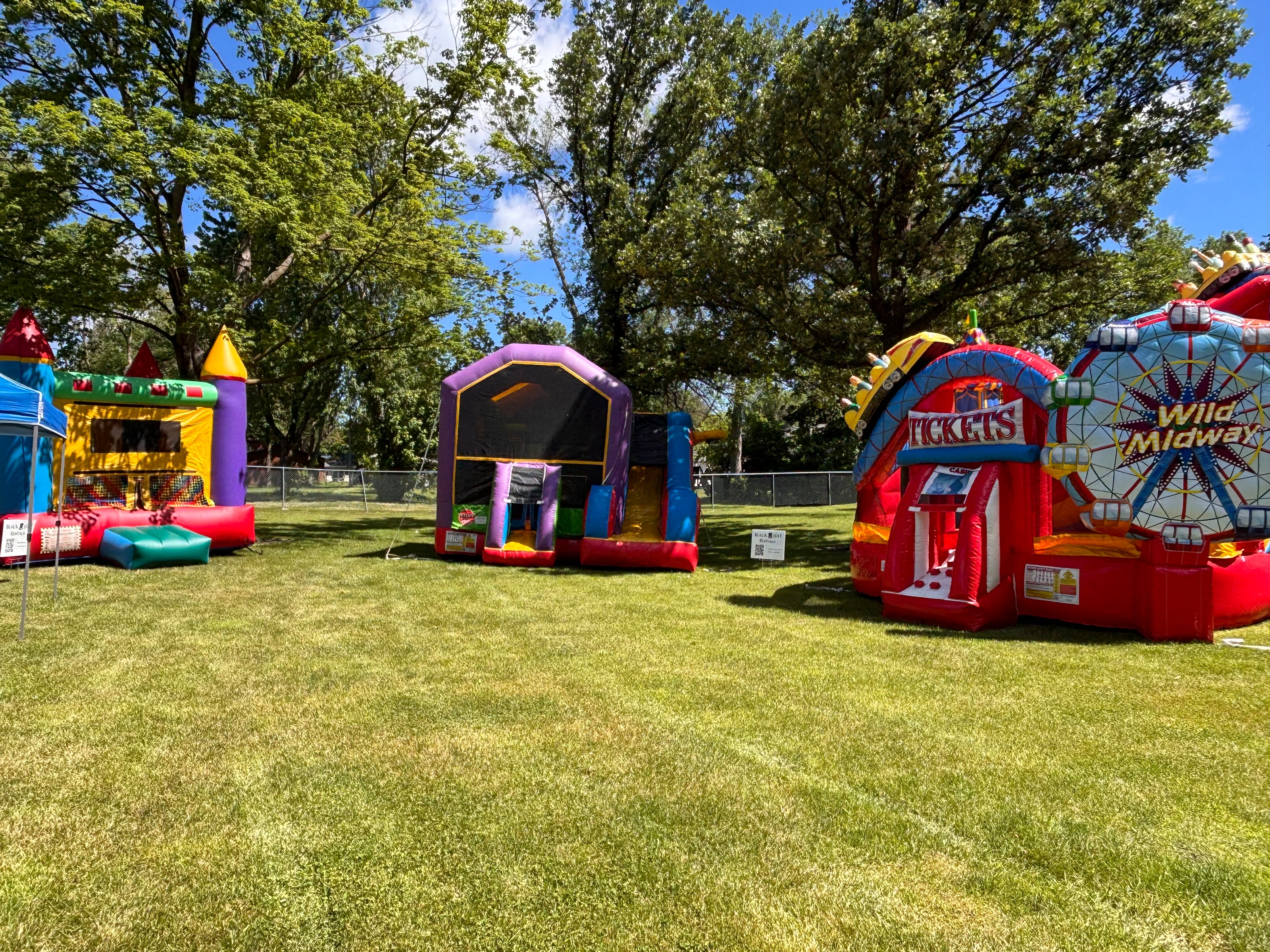 Colorful inflatable playground equipment on a grassy field with trees in the background