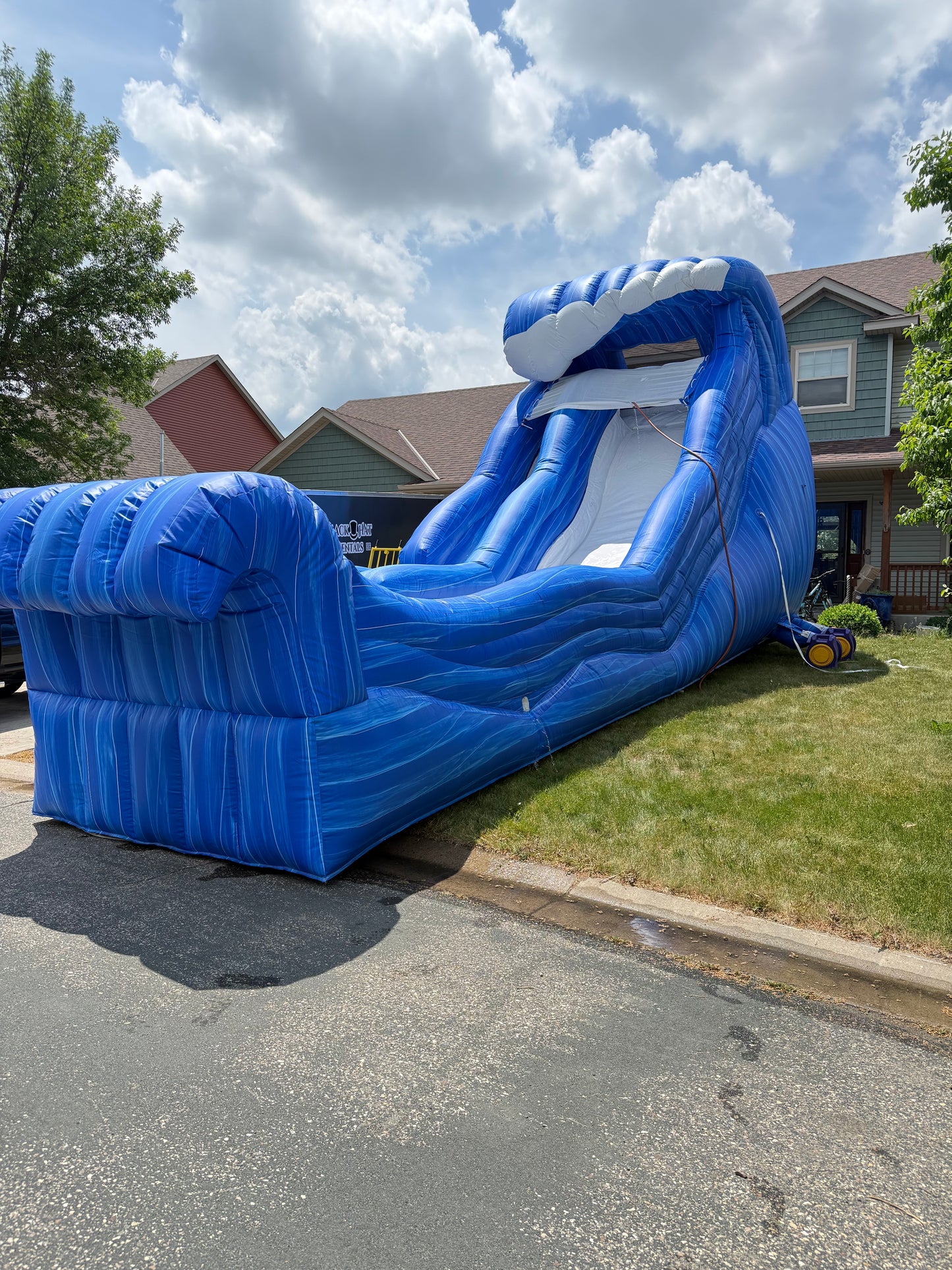 Large blue inflatable slide on a residential street with houses and trees in the background.