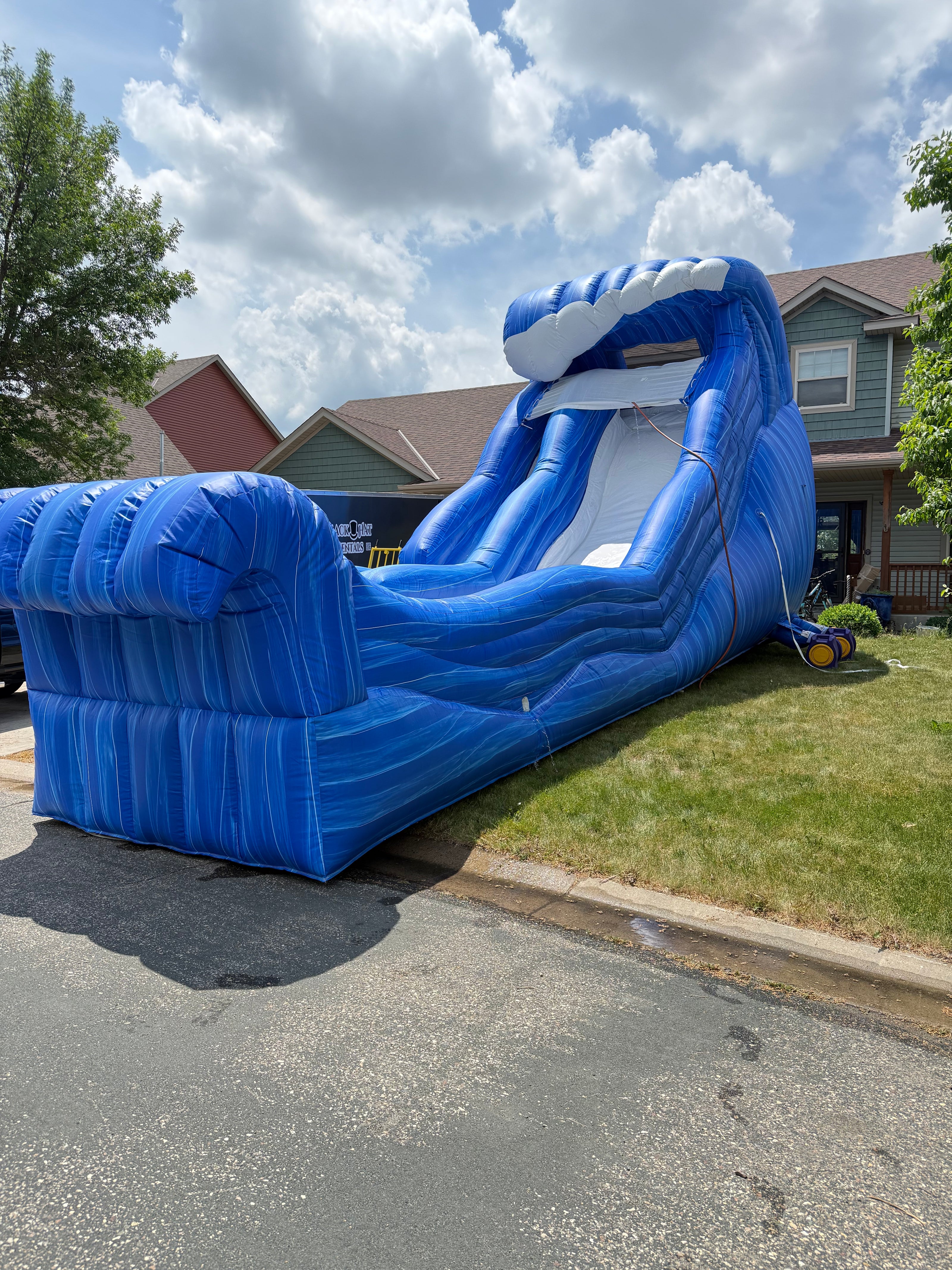 Large blue inflatable slide on a residential street with houses and trees in the background.