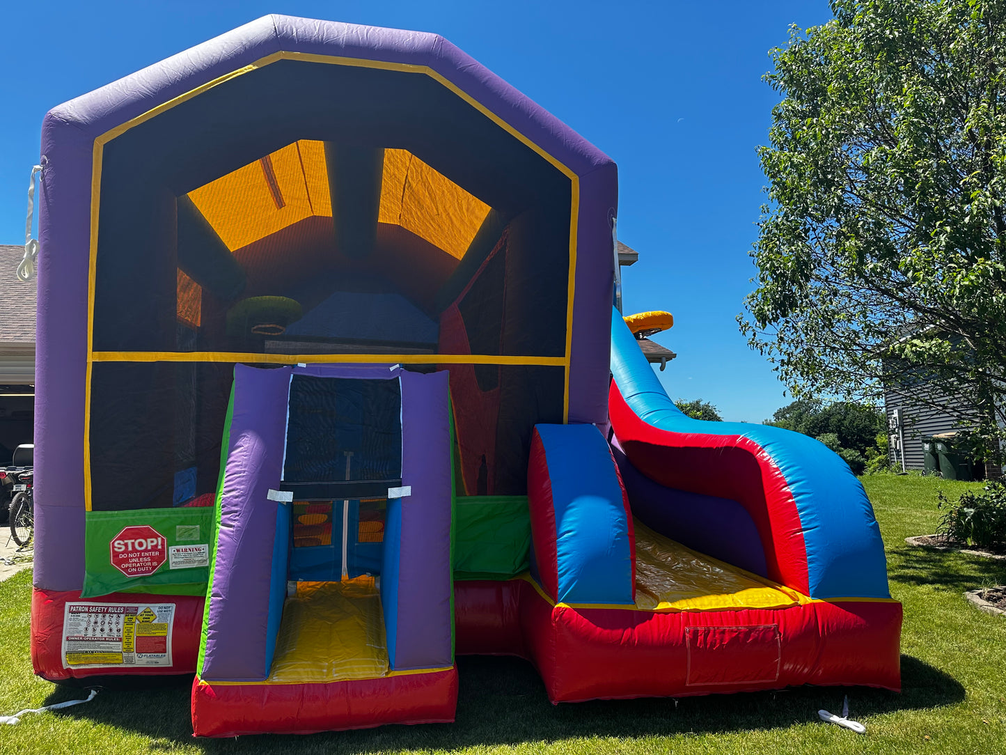 Vibrant bounce house with slide set up on a green lawn, featuring colorful panels and a secure entrance, perfect for kids' parties and events.