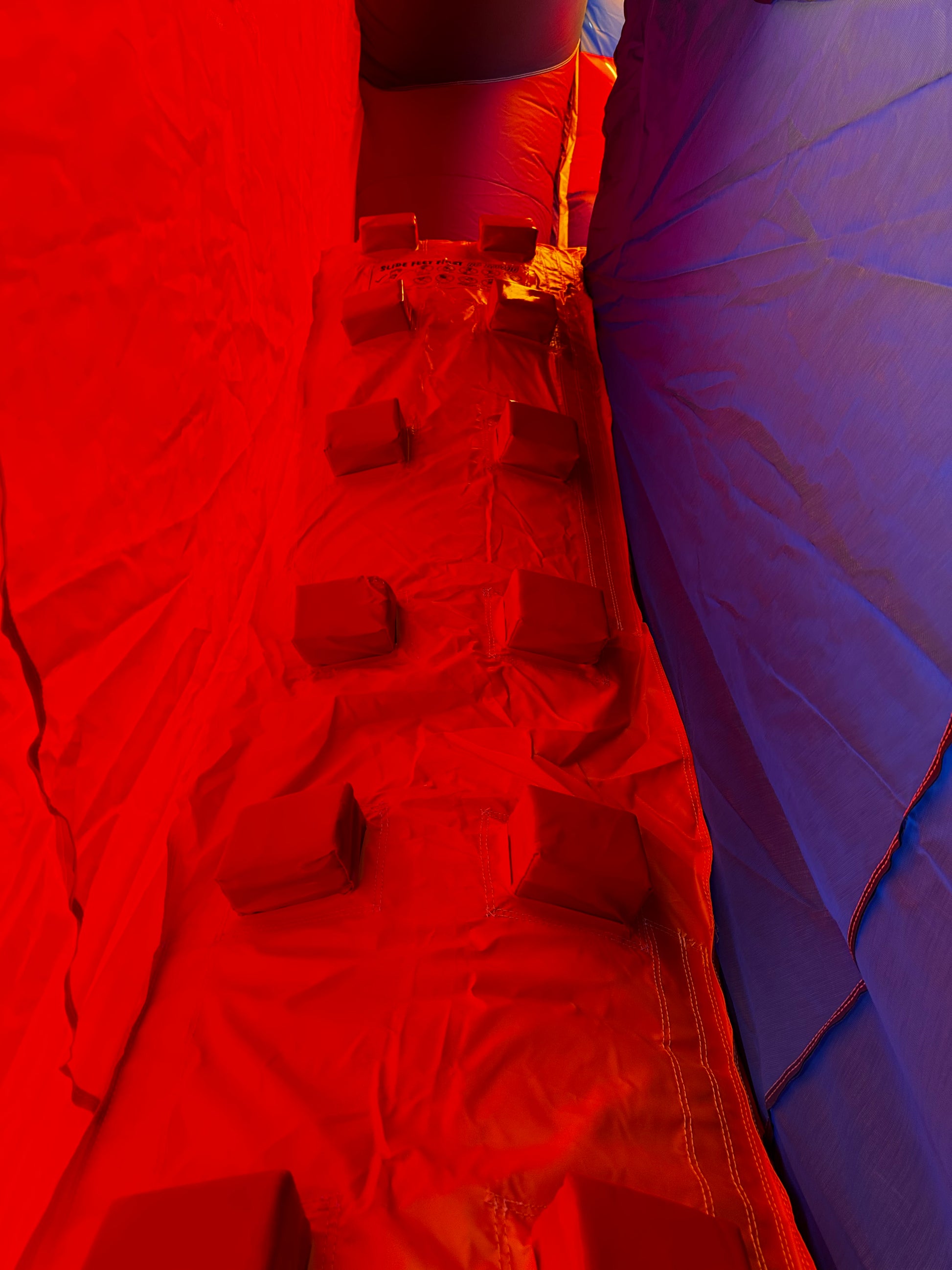 Interior view of a bounce house slide's climbing wall with bright red and blue colors, padded steps, and secure, durable stitching.