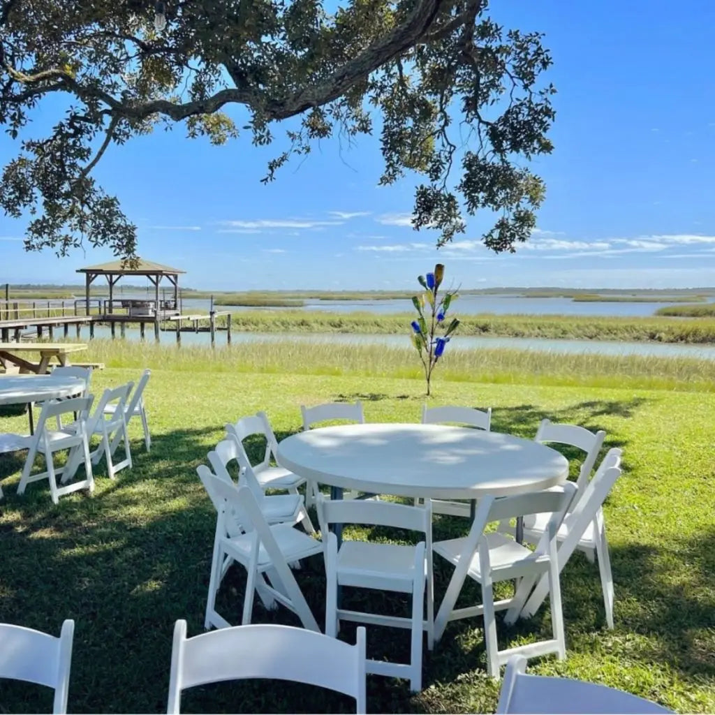 White folding chairs and round tables set up on a lush green lawn, perfect for outdoor weddings and events, creating a picturesque setting.