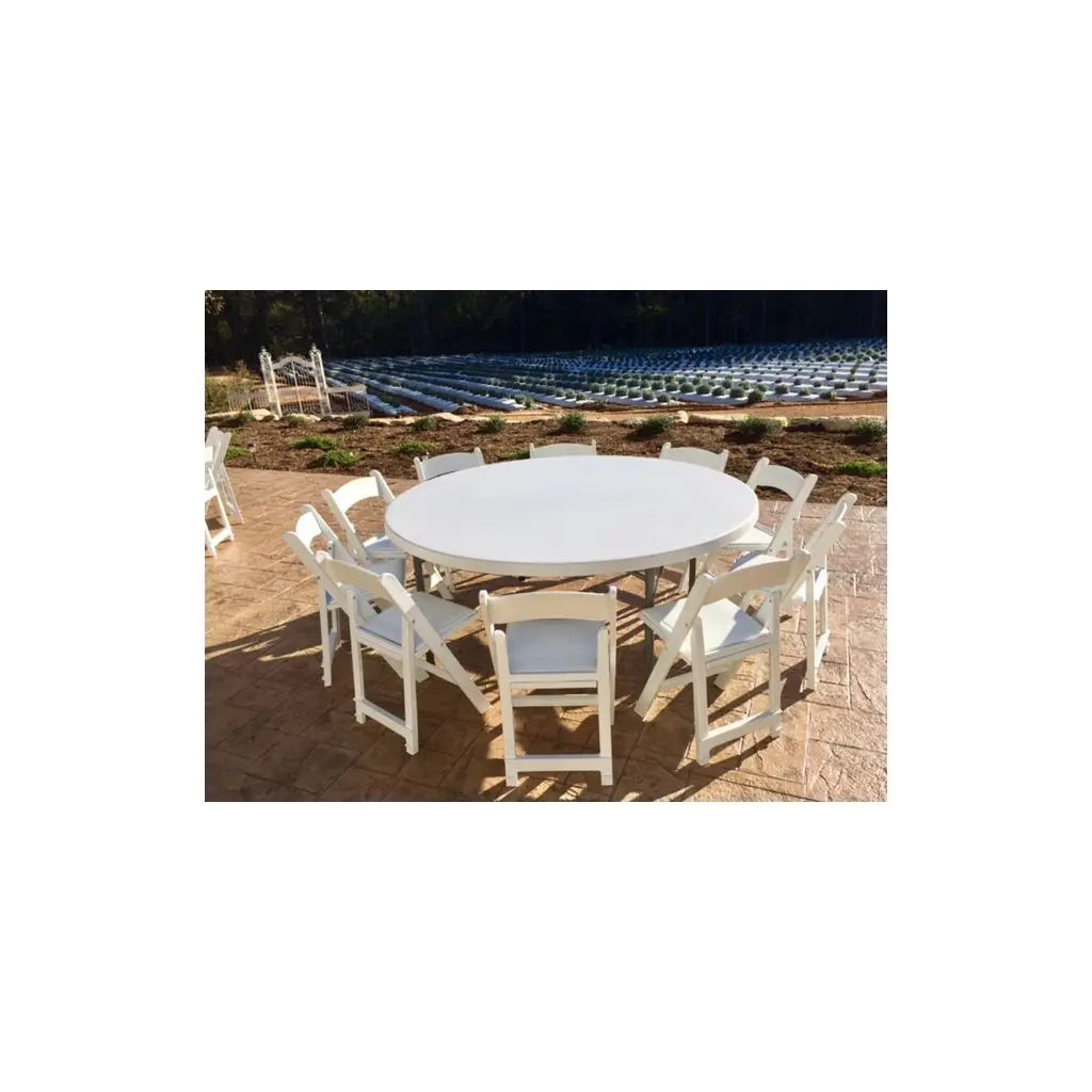 White folding chairs and round tables set up on a lush green lawn, perfect for outdoor weddings and events, creating a picturesque setting.