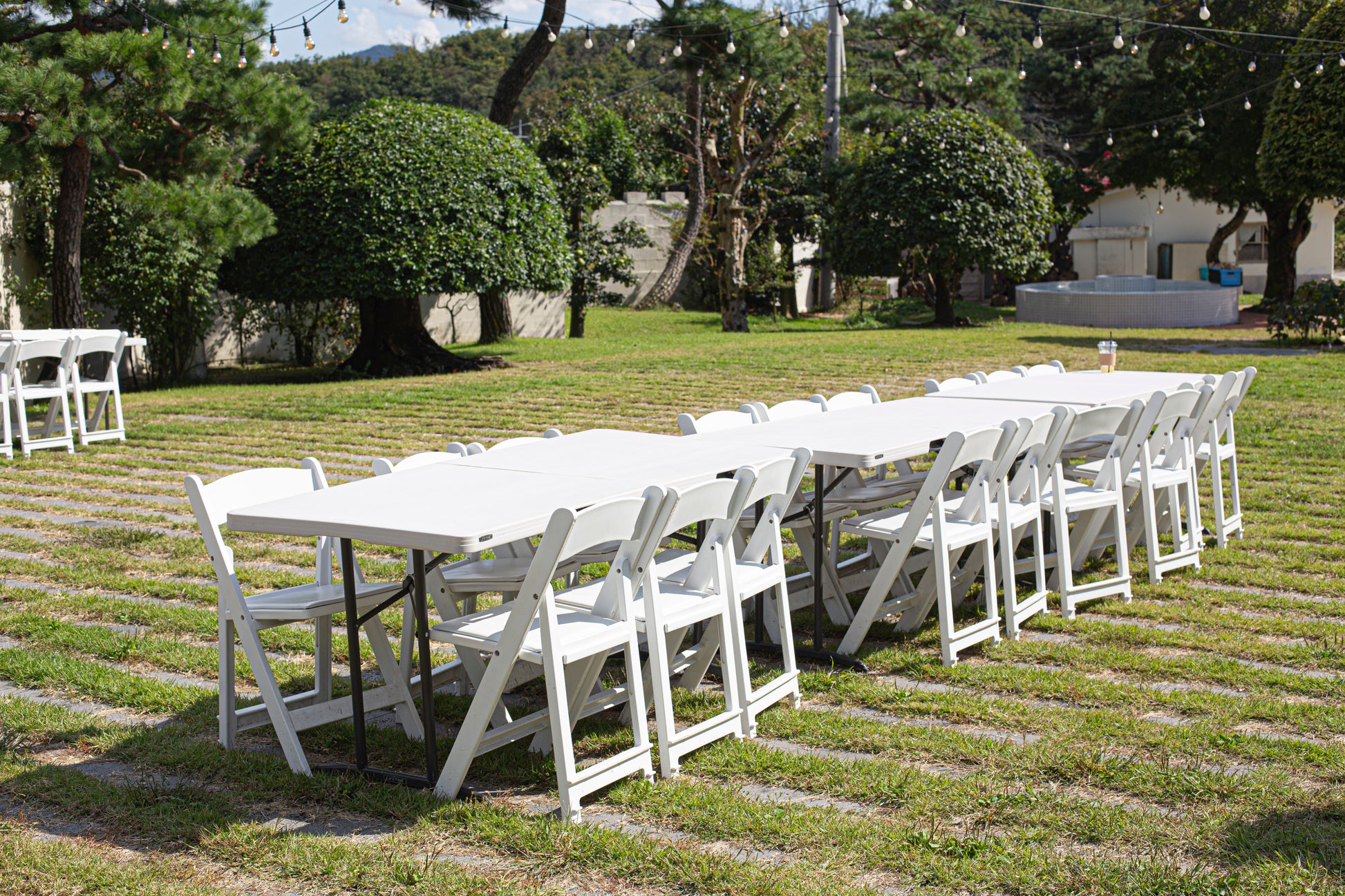 White folding chairs and banquet tables set up on a lush green lawn, perfect for outdoor weddings and events, creating a picturesque setting.